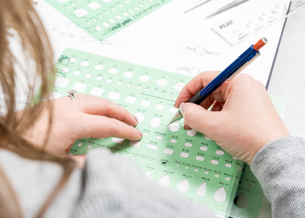 Person using a green ruler with white dots and a blue pencil on a white surface.